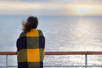Back of woman wrapped in plaid standing on cruise liner deck
