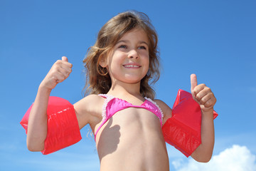 little happy girl with red inflatable armbands thumbs up