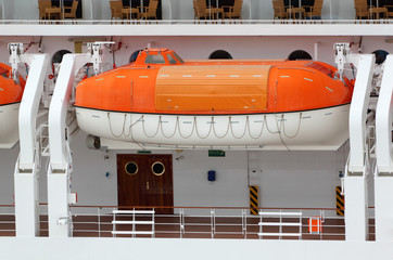 Orange lifeboat installed on large white passenger liner deck