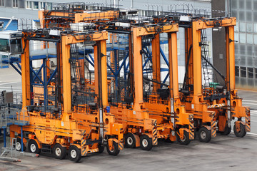 Many empty large orange loaders stand on asphalt in seaport