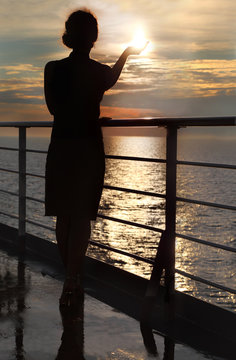 dark silhouette of woman holding sun and standing on deck