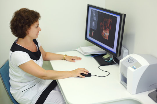 Dentist carefully looks skull X-rays at computer monitor