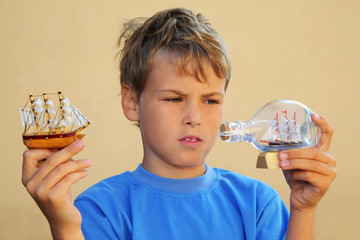 Boy holds small model of sailing ship and ship in bottle