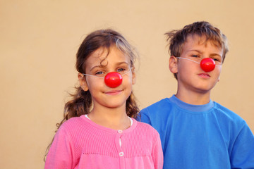 Brother and sister with red clown noses stand near wall