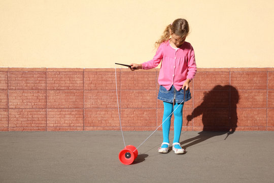 Beautiful little girl plays with yo-yo on sunny day outdoor.