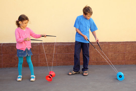 Brother and sister play with yo-yo toy at sunny day outdoor.