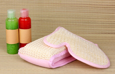 Bottles with scrub and sponges on bamboo background