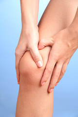 woman holding sore knee, on blue background