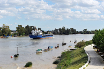 Naklejka premium Barco mercante navegando por el río Guadalquivir desde el puerto de Sevilla hacia el Oceano Atlántico