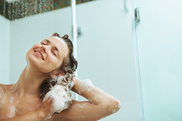 Happy woman washing hair with shampoo under water jet - obrazy, fototapety, plakaty