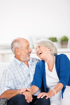 älteres paar sitzt lachend auf dem sofa