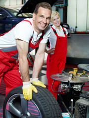 Two motor mechanics fitting a summer tyre in a garage
