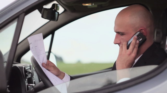 Angry businessman with cellphone and paperwork in the car