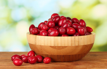 fresh cornel berries in wooden bowl on green background