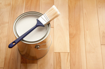 Paintbrush and a can of white paint on wooden floor