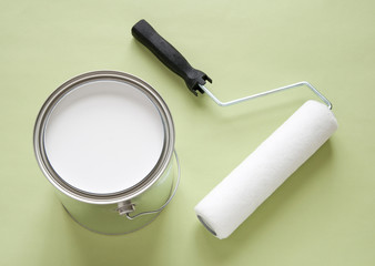 Can of white paint and roller on green background