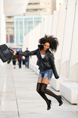 Young pretty black woman jumping in the street with a briefcase