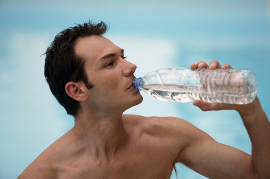 Shirtless man drinking from water bottle