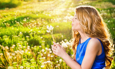 Girl blowing on white dandelion in the field in a autumn day