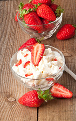 Cottage cheese and strawberries in white bowl on wooden surface.