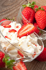 Cottage cheese and strawberries in white bowl on wooden surface.