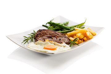 Grilled steaks, French fries, fried egg and vegetables