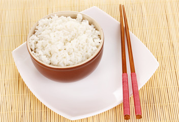 Bowl of rice and chopsticks on plate on bamboo mat