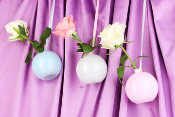 Beautiful roses in vases hanging on cloth background