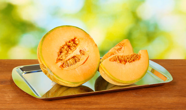 Cut melon on metal tray on green background close-up