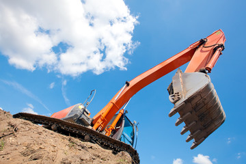 Fototapeta premium Excavator standing in a ground with raised bucket over sky