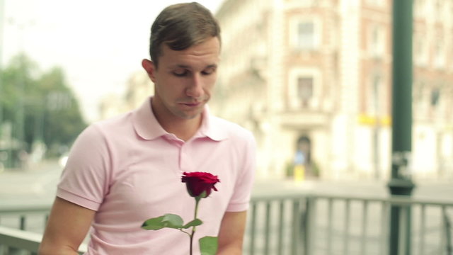 Young man with rose waiting for his date in the city