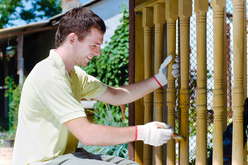 Young man painting wooden fence in the garden