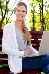 smiley blonde sitting in park with laptop