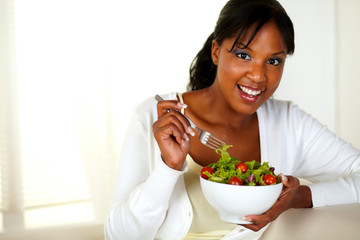 Young female looking at you while eating salad