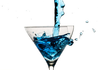 Ice cubes and martini glass filled with blue liqueur on white ba
