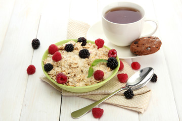 tasty oatmeal with berries and cup of tea, on white wooden