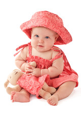 Smiling baby girl in pink dress and sun hat sits and plays with