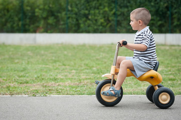 Four year old kid playing outdoor on tricycle.