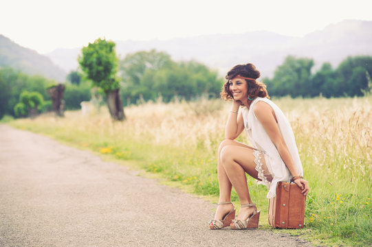 Beautiful girl waiting on a country road with her suitcase.