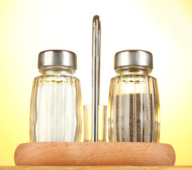 Salt and pepper mills, on wooden table on yellow background