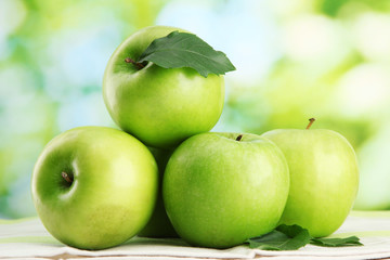 Ripe green apples with leaves, on table, on green background