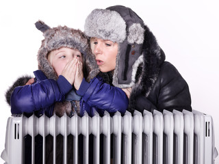 Mother and daughter in warm winter coats leaning over a radiator