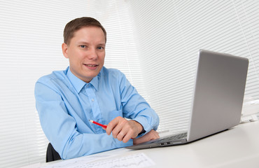 Young businessman working in office, sitting at desk with laptop