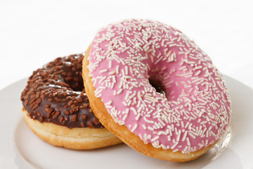 Pink and chocolate donuts with sprinkles on a plate