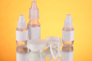 Eye drops and lenses on orange background