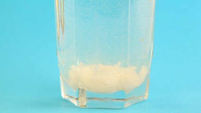 Sugar is dissolve in glass of warm water on blue background