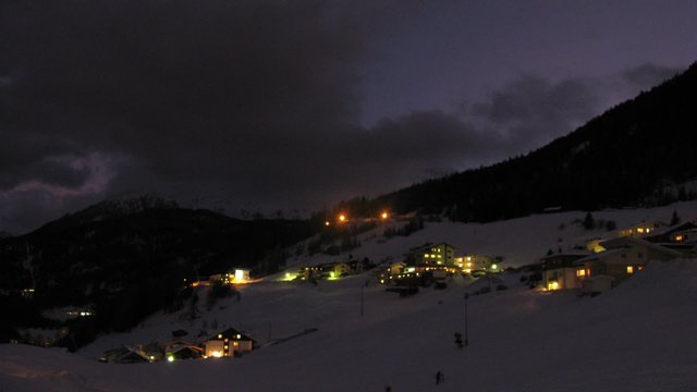 Snowplow goes near hotels in valley at night