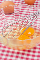 Whisk in bowl with eggs on checked cloth