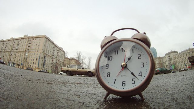 Clocks stands on roadside of road in front of moving cars