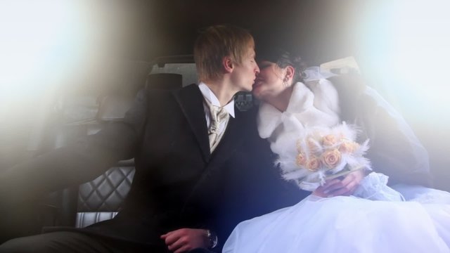 Newly-married couple sits together in limousine and kisses